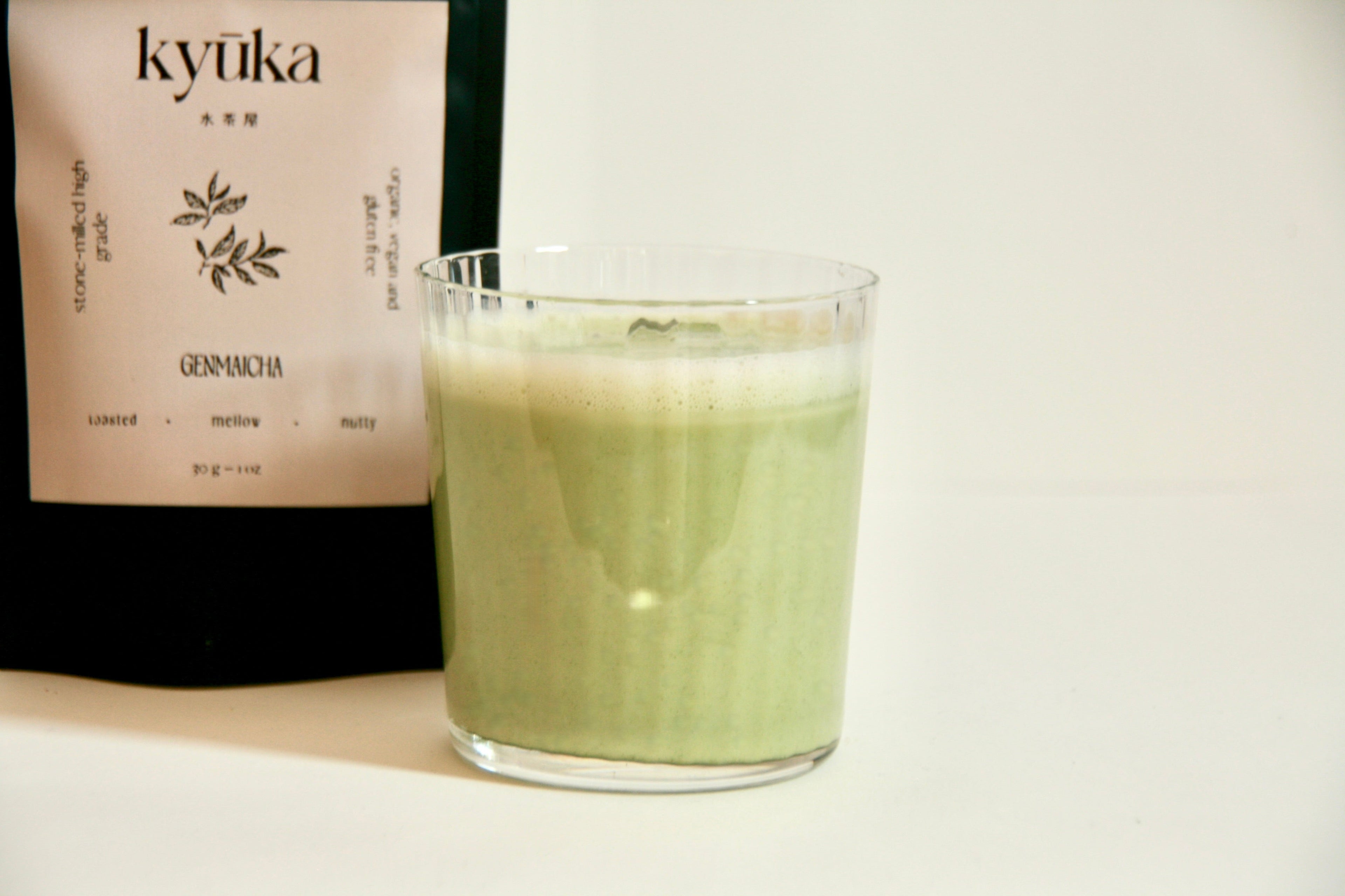 Glass of creamy Kyuka Genmaicha with froth, next to Kyuka Matcha tea package